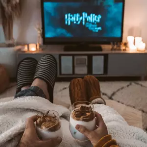 Paar sitzt zugedeckt auf dem Sofa mit heißer Schokolade in der Hand beim Fernsehen