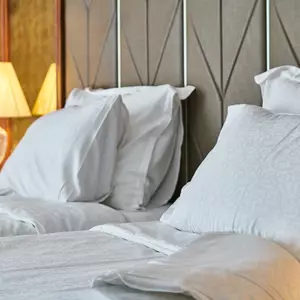 Aufgebettetes Doppelbett mit Muster im Kopfteil und angeschalteter Nachttischlampe