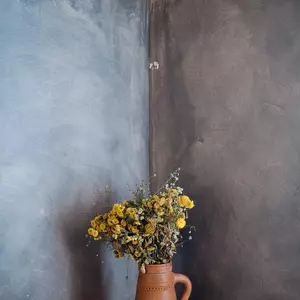 Blumenstrauss in Tonvase auf rundem Holztisch in der Ecke vor einer blau marmorierten Wand