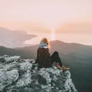 Junge Frau in Abenddämmerung sitzend auf einem Felsen mit Blick auf die untergehende Sonne