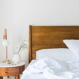 Holzbett mit Kopfkissen, zerknüllter Bettdecke und Nachttisch