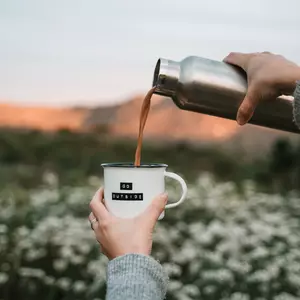 Detailaufnahme einer Blechtasse, in die gerade heisser Tee geschüttet wird, vor einem Bergpanorama